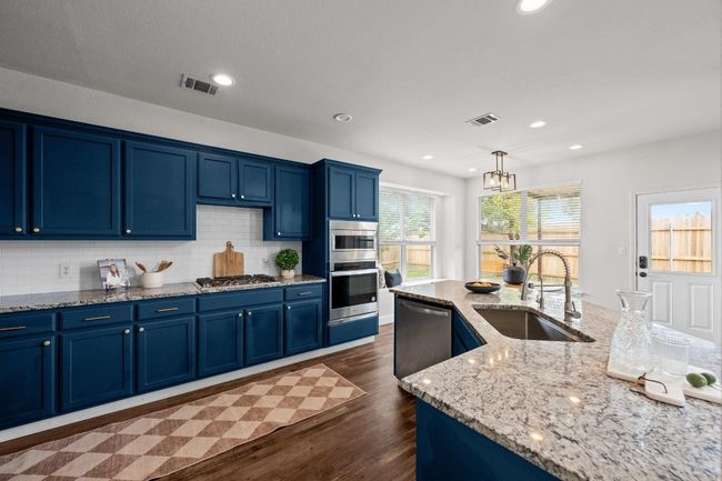 Kitchen featuring stainless steel appliances, a sink, blue cabinetry, dark wood-type flooring, and tasteful backsplash | Image 6