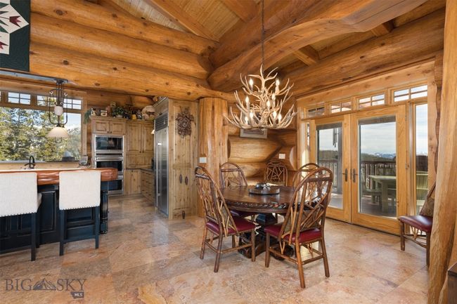 Main level dining room to kitchen, featuring custom antler chandelier, inlaid turquoise table, an abundance of natural lighting, cathedral ceiling and french doors to vast exterior deck. | Image 35