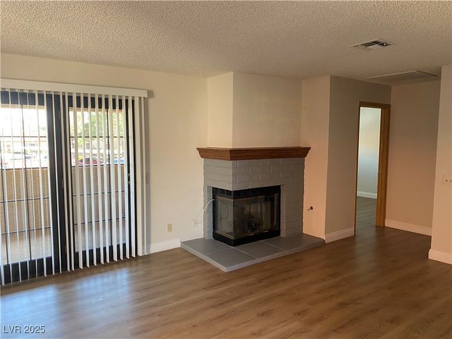 Unfurnished living room featuring a textured ceiling, wood finished floors, a brick fireplace, and baseboards | Image 4