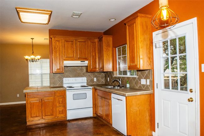 Kitchen featuring white appliances, under cabinet range hood, and brown cabinetry | Image 6