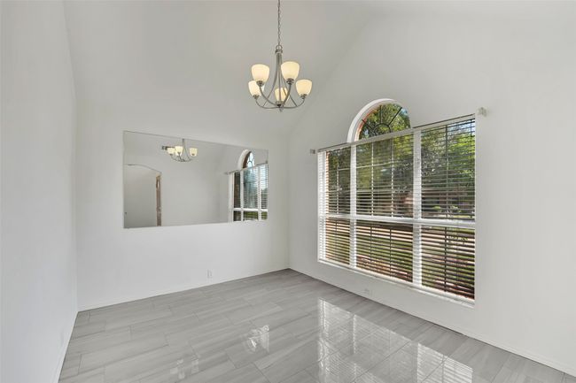 Spare room featuring an inviting chandelier, high vaulted ceiling, and light tile floors | Image 5