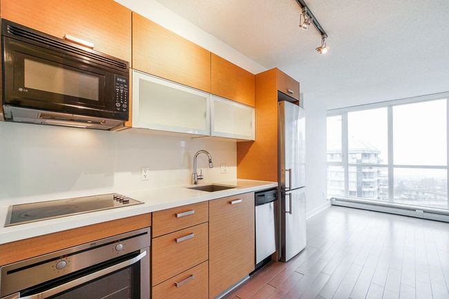 Kitchen with wood finished floors, a baseboard radiator, light countertops, black appliances, and a sink | Image 4
