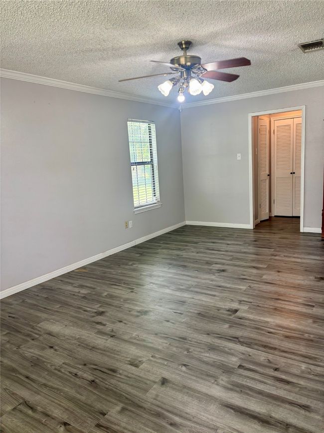Empty room featuring ornamental molding, ceiling fan, a textured ceiling, and dark wood-style flooring | Image 13