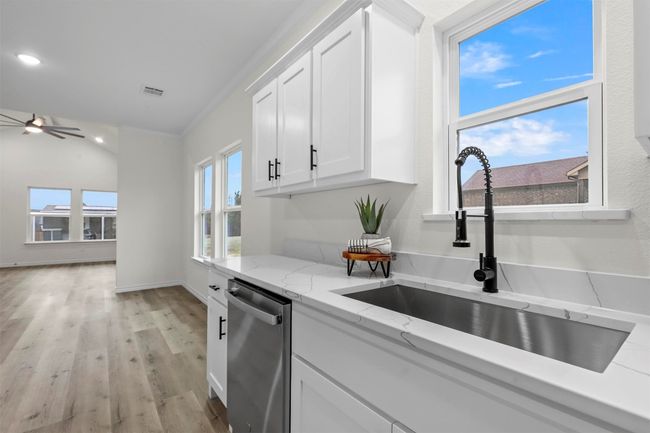 Kitchen featuring sink, light stone counters, white cabinetry, dishwasher, and ceiling fan | Image 19