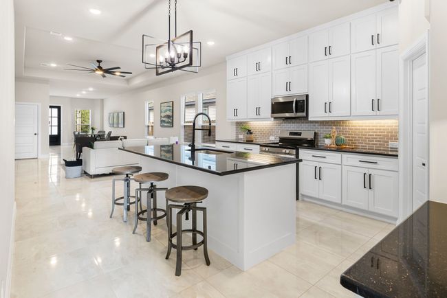 Kitchen featuring a tray ceiling, decorative backsplash, ceiling fan with notable chandelier, stainless steel appliances, and a sink | Image 8