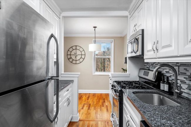 Kitchen with stainless steel appliances, white cabinets, tasteful backsplash, crown molding, and light wood finished floors | Image 11