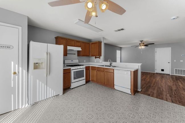Kitchen featuring ceiling fan, white appliances, a peninsula, light countertops, tile floor, and brown cabinets | Image 8
