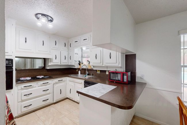 Kitchen with a peninsula, dark countertops, white cabinetry, a sink, and black appliances | Image 11