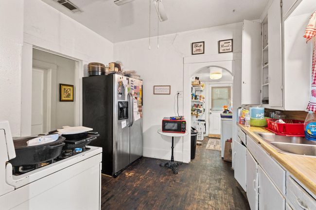 Kitchen with stainless steel fridge, white cabinets, dark wood finished floors, a ceiling fan, and light countertops | Image 7