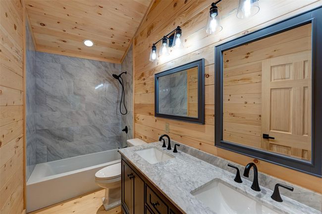 Bathroom featuring double vanity, bathtub / shower combination, toilet, wood walls, and wooden ceiling | Image 28