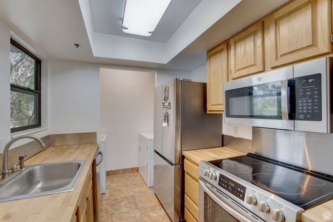 Kitchen featuring sink, wooden counters, stainless steel appliances, a tray ceiling, and light brown cabinetry | Image 10