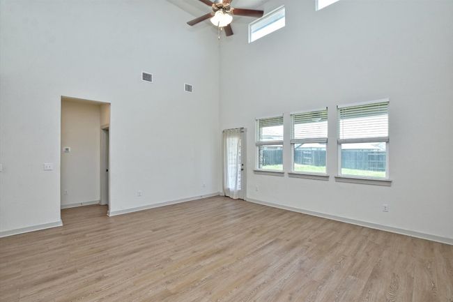 Empty room with a high ceiling, a ceiling fan, light wood-style flooring, and baseboards | Image 9
