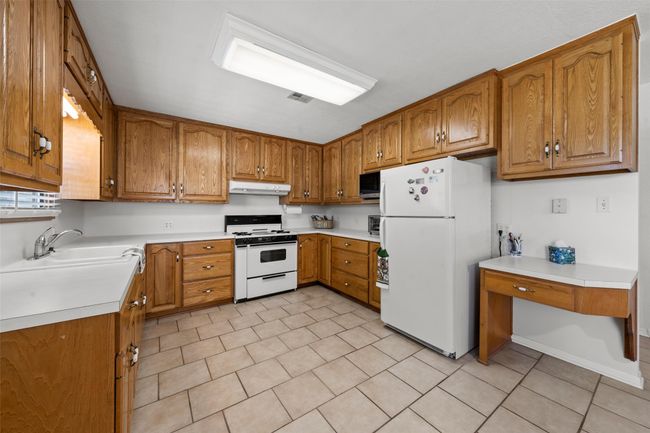 Kitchen with white appliances, under cabinet range hood, brown cabinets, light countertops, built in desk | Image 6