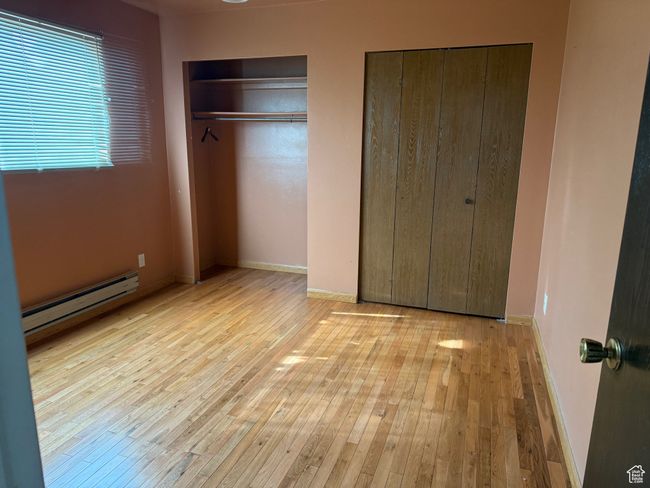 Unfurnished bedroom featuring hardwood / wood-style flooring, a baseboard radiator, baseboards, and two closets | Image 16
