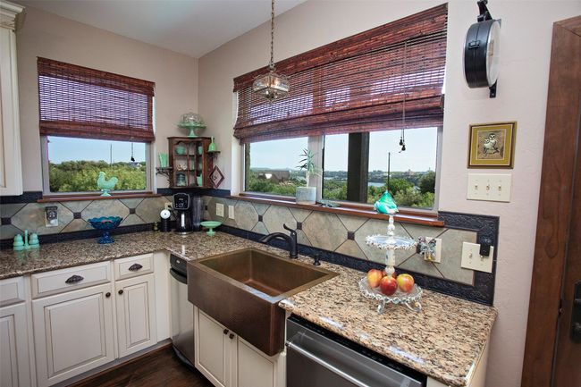 Kitchen with stainless steel dishwasher, decorative backsplash, light stone counters, white cabinets, and hanging light fixtures | Image 18