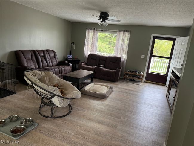Living room with ceiling fan, light wood-style floors, and a textured ceiling | Image 6