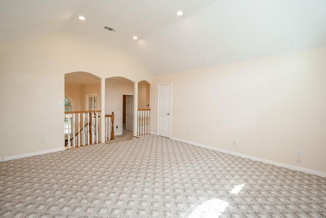 This spacious room features plush patterned carpet, neutral walls, and recessed lighting. It includes a doorway and railing leading to a stairway, adding an open and airy feel. | Image 32