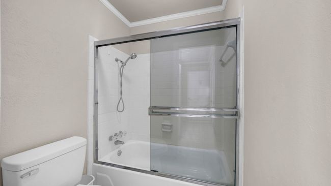 Bathroom featuring toilet, bath / shower combo with glass door, and ornamental molding | Image 25