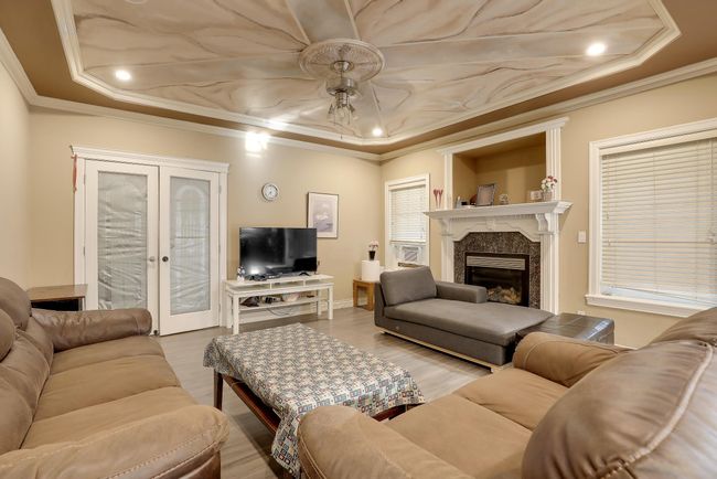 Living room featuring a fireplace, a raised ceiling, a ceiling fan, ornamental molding, and french doors | Image 14