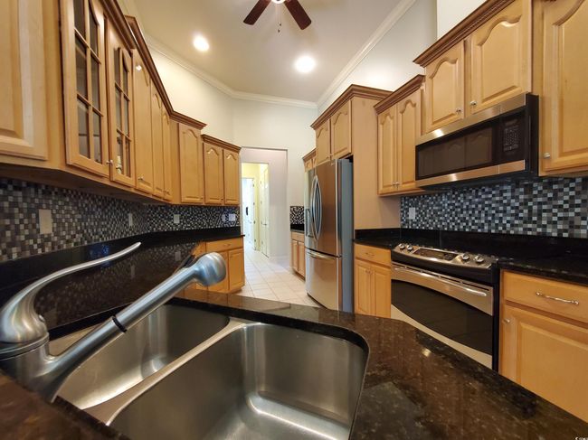 An abundance of cabinets, roll-out shelves, a glass display cabinet, a ceiling fan, and a 2-3 seat Breakfast Bar | Image 8