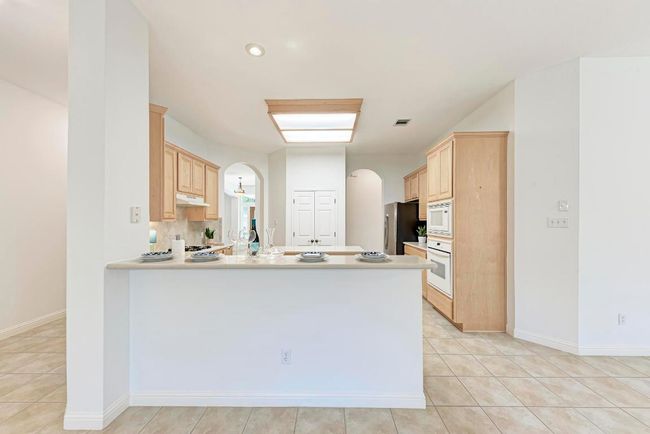 Kitchen featuring visible vents, arched walkways, light brown cabinets, white appliances, and under cabinet range hood | Image 15