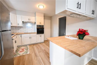 Kitchen with black oven, light wood-type flooring, white cabinetry, and stainless steel refrigerator | Image 2