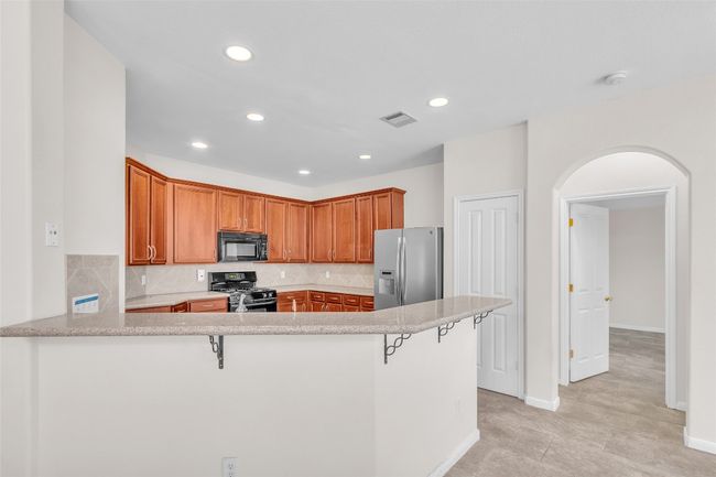 Kitchen with backsplash, a peninsula, a breakfast bar area, black appliances, and recessed lighting | Image 10