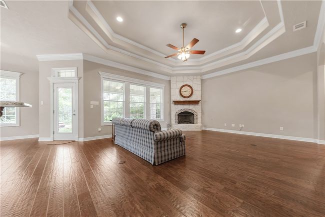 Living room featuring a tray ceiling, a ceiling fan, a fireplace with raised hearth, hardwood / wood-style flooring, and ornamental molding | Image 4