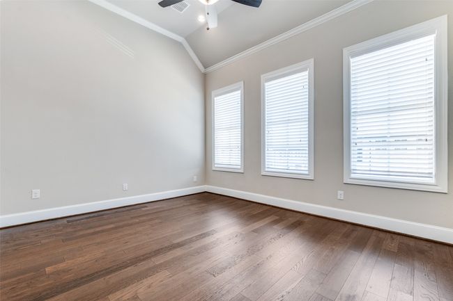 Empty room with ornamental molding, lofted ceiling, ceiling fan, and dark wood-type flooring | Image 25