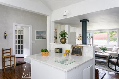 Kitchen with white cabinets, light stone countertops, a wood stove, wood flooring, and lofted ceiling | Image 3