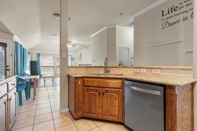 Kitchen featuring stainless steel dishwasher, light tile patterned flooring, brown cabinetry, vaulted ceiling, and crown molding | Image 17