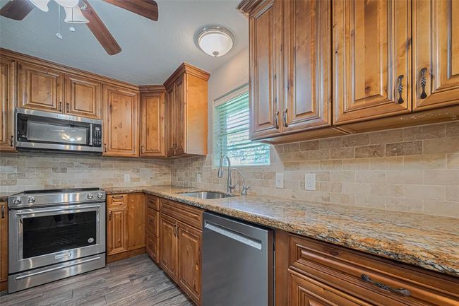 Updated kitchen offers pull out drawers, custom cabinets with soft close, stainless-steel appliances, and elegant granite countertops. Features a tile backsplash, a large sink, and ample natural light from the window, that overlooks the lush backyard | Image 11