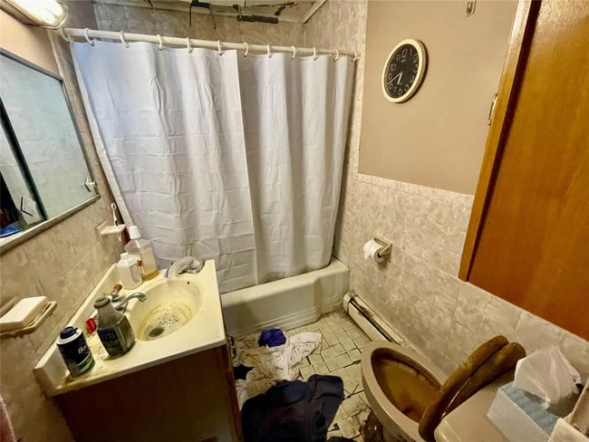 Bathroom with shower / bath combination with curtain, tile walls, a baseboard radiator, vanity, and tile patterned flooring | Image 21