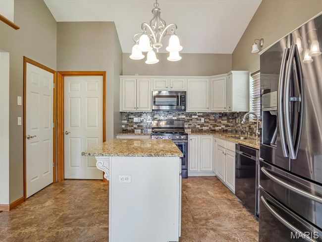 Kitchen featuring stainless steel appliances, granite counter tops, a chandelier, decorative backsplash, vault ceiling, and white cabinets | Image 12