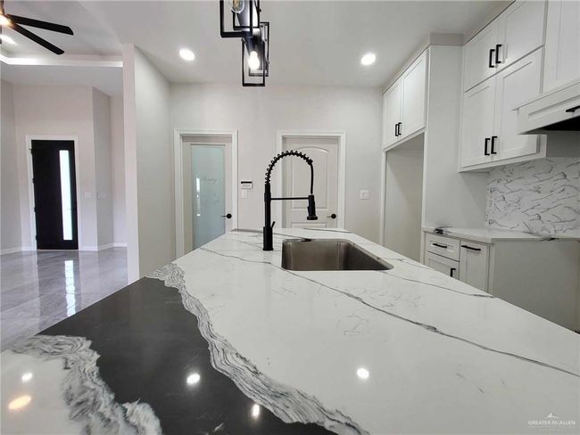Kitchen with decorative backsplash, sink, light stone countertops, white cabinets, and ceiling fan | Image 11
