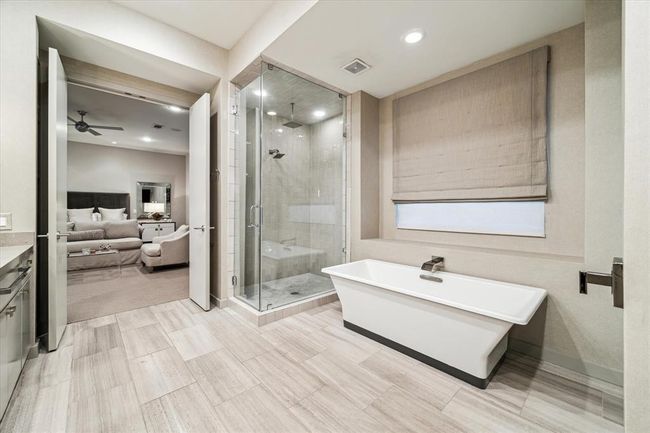 Closer view of the Primary Bath with its striking rectangular tub with wall mounted designer fixtures - all set against an oversized window with Roman shade. Also notice the adjacent walk-in shower with glass surround. | Image 24