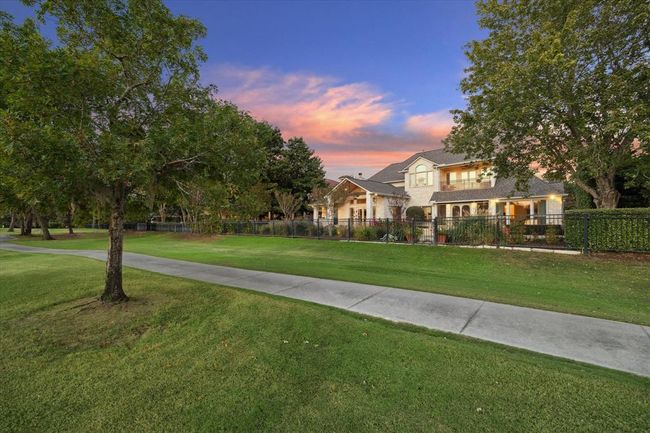 This photo showcases a beautiful two-story home with a charming porch, set amidst lush greenery and mature trees. The property is fenced and features a well-maintained lawn, creating a serene and inviting atmosphere. | Image 35