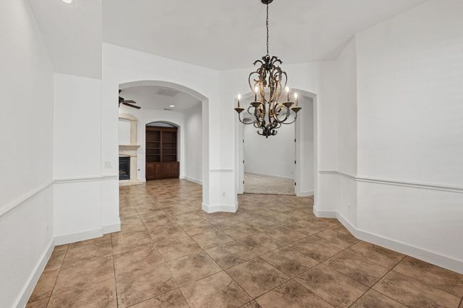 Unfurnished dining area with a chandelier, a fireplace with raised hearth, arched walkways, light tile patterned floors, and a ceiling fan | Image 7