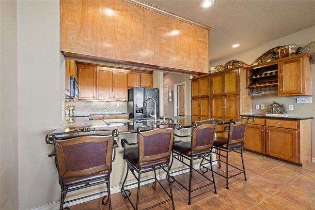Kitchen featuring a breakfast bar area, a peninsula, black fridge, backsplash, and brown cabinets | Image 10