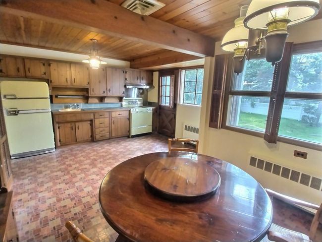 Kitchen featuring white appliances, radiator heating unit, wooden ceiling with exposed beams, under cabinet range hood, and a sink | Image 12