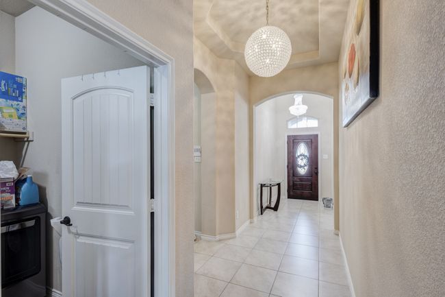 Entrance foyer with arched walkways, a chandelier, light tile patterned floors, a textured wall, and baseboards | Image 4