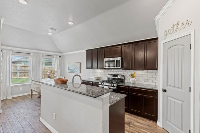 Kitchen featuring stainless steel appliances, lofted ceiling, a center island with sink, granite countertops, and dark brown cabinetry | Image 26