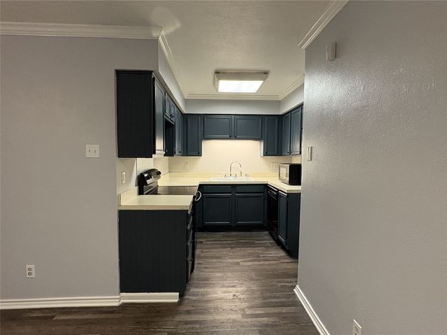Kitchen with ornamental molding, light countertops, black appliances, dark wood-type flooring, and dark cabinetry | Image 9