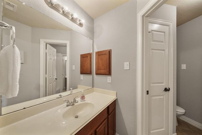 Serving as the home's third full bath, this bath is accessible from the fourth & fifth bedrooms as well as the corridor offering convenient access from the game room. Features include a private dressing area with a wood-stained cabinet and solid surface counter top, wall mounted mirror with lighting above, a built-in medicine cabinet and semi-private access to a shared water closet. | Image 38