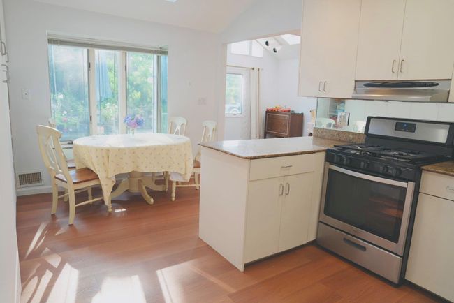 Kitchen featuring stainless steel range with gas stovetop, under cabinet range hood, lofted ceiling, light wood-style floors, and a peninsula | Image 6