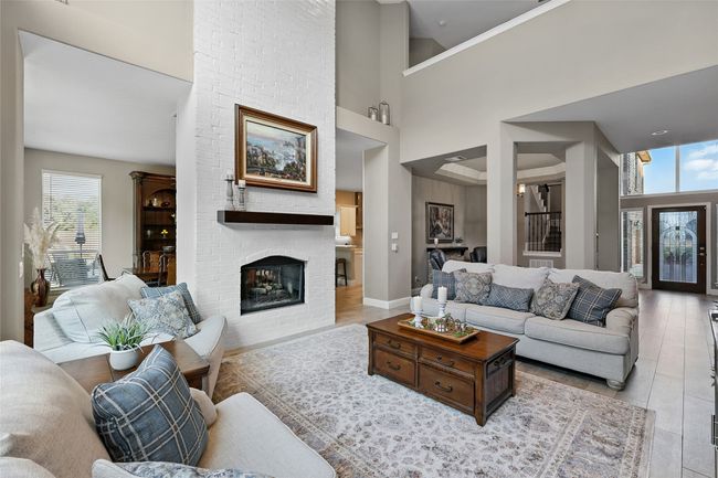 Living room with healthy amount of natural light, a high ceiling, wood -like ceramic tile floors, and a brick see through fireplace | Image 9