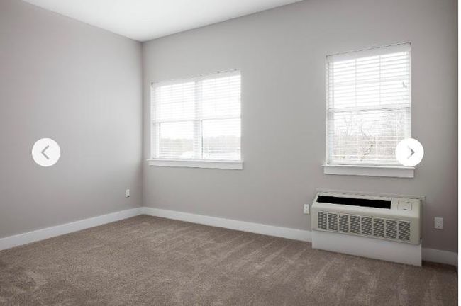 Empty room with carpet floors, baseboards, and an AC wall unit | Image 4