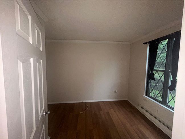 Unfurnished room featuring wood finished floors, healthy amount of natural light, crown molding, and a baseboard heating unit | Image 6