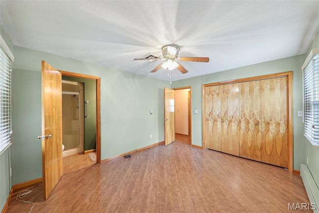 Unfurnished bedroom with a baseboard heating unit, wood finished floors, a closet, ceiling fan, and ensuite bathroom | Image 22
