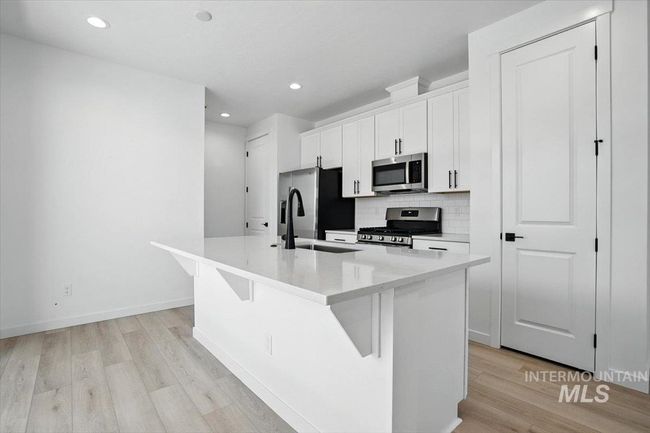 Kitchen with stainless steel appliances, a kitchen island with sink, light wood-type flooring, backsplash, and white cabinets | Image 8